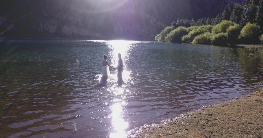 Couple of newlyweds kissing and hugging in the lake after their marriage. Silhoette of the groom and the bride inside the lake at sunset. 4k	