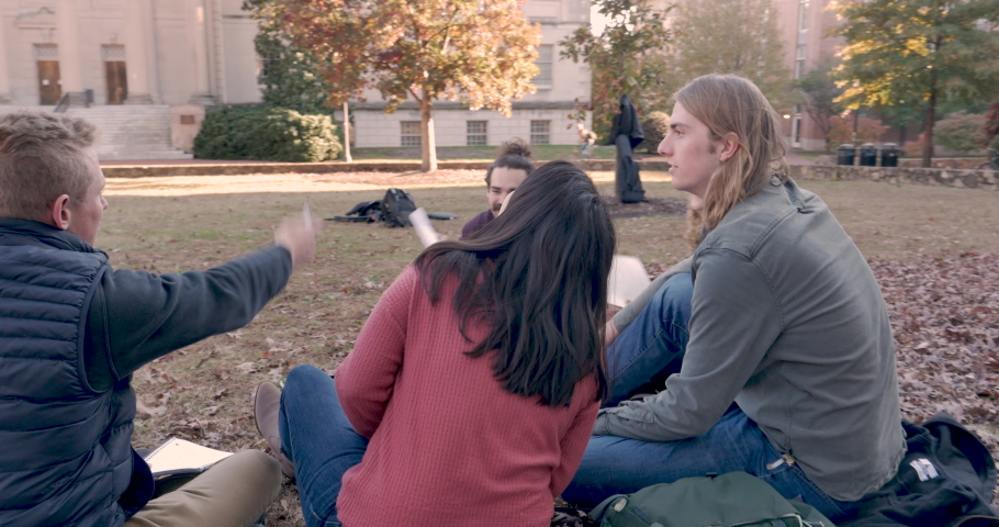 Camera circles around a group of college students studying outside with paper notebooks during the fall semester on campus