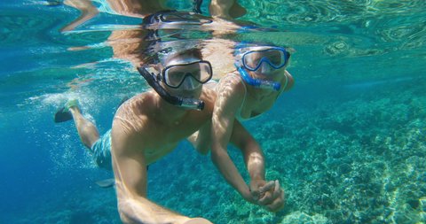 POV shot of young attractive couple snorkeling together holding hands in tropical ocean water with fish, summer vacation fun