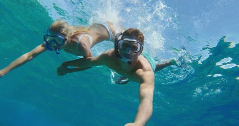 POV shot of young attractive couple diving down and snorkeling together in tropical ocean water, summer vacation fun