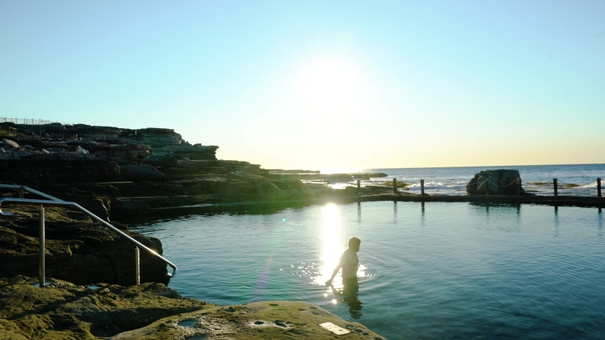 Panning Shot of a man Wading through a stunning Rock Pool at Sunrise