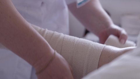 Nurse bandages a patient's leg with an elastic bandage in a hospital bed