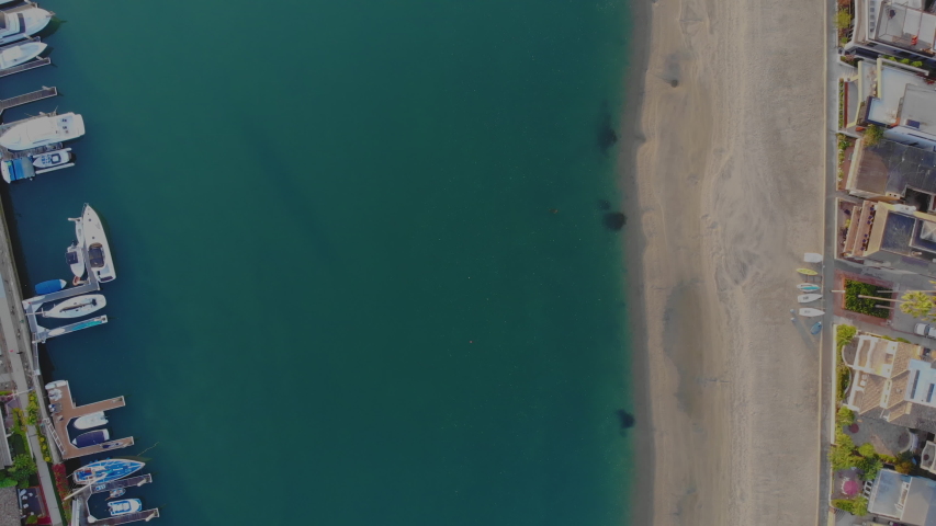 Birds eye view of the Naples Canals and Alamitos Bay in the Naples neighborhood of Long Beach, CA featuring turquoise water, yachts, boats, kayak and a sandy beach.