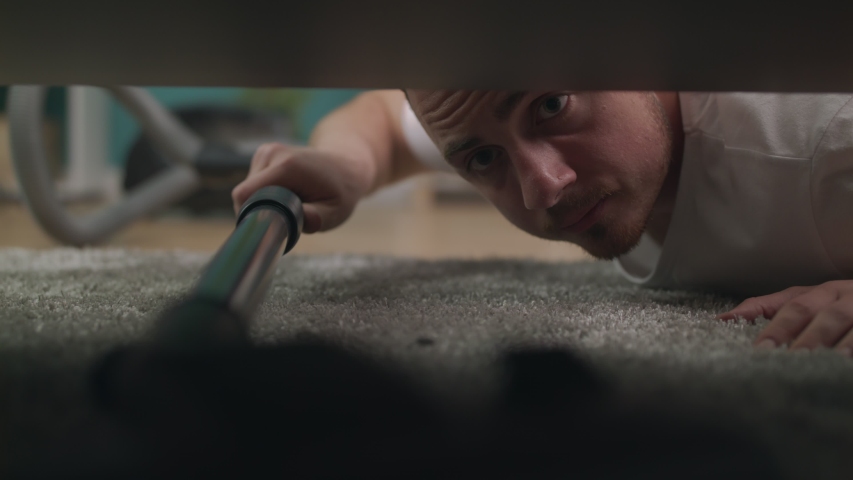 Young man cleaning a floor under a bed lying on the floor using vacuum cleaner Royalty-Free Stock Footage #1029521204