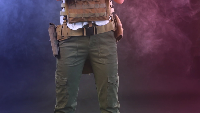 Woman in protective armour and headphones holds gun in hands, posing over dark smoky background. Army, dedication, weapon, technology.