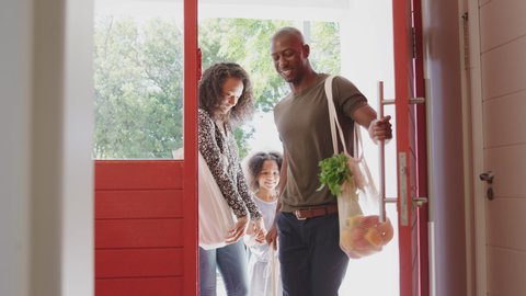 Family Returning Home From Shopping Trip Using Plastic Free Grocery Bags Opening Front Door