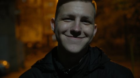 positive young man standing on the street with orange illumination at night. Urban portrait of joyfull guy