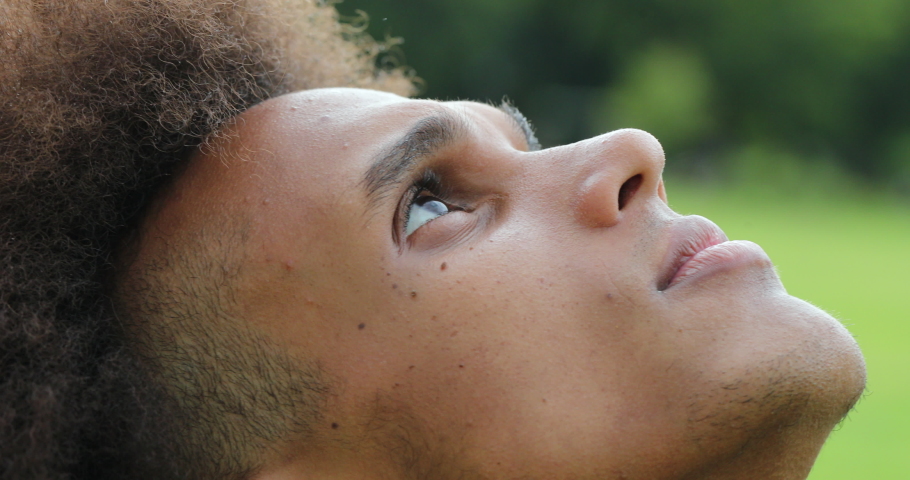 Young african man closing and opening eyes, looking up to sky with faith and hope