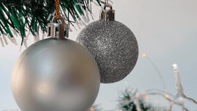 Christmas background, seamless looped video: silver Christmas ball hanging and swinging, led garlands with white and small yellow lights on white background. Christmas decorations, 4k