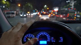 Driving a car through the city POV , hand on steering wheel close up. Dusk, Night, early or late. Traffic jam. Many cars with light on.
