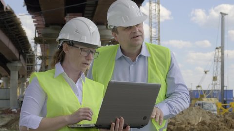 Closeup of man and woman working on background of construction overpass. Builders discussing future work plan for erection of bridge using computer.
