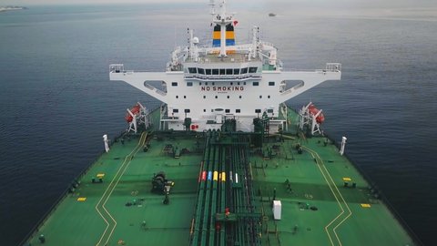 Green deck tanker ship underway in open water. Aerial, flying over. Ship's navigation bridge or superstructure showing radar electronics, lifeboat, no smoking and safety first signs on an oil tanker
