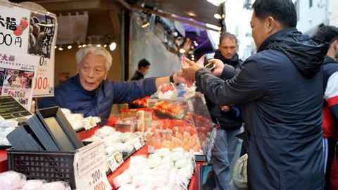 Tokyo, Japan - March 31, 2019: Street in Tsukiji near Ginza with people in busy market talking ordering buying mochi dessert from vendor in Japanese