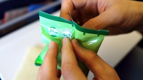 Tokyo, Japan - March 28, 2019: Man hands trying struggling to open Japanese snack food on airplane ANA flight with gluten-free halal rice crackers