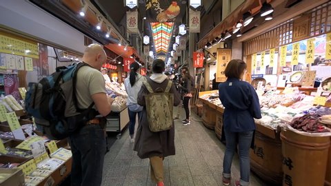 Kyoto, Japan - April 16, 2019: Street with many people walking inside Nishiki market by food vendors merchants in slow motion