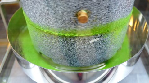 Matcha green tea grinding stone machine in motion with vibrant colorful powder closeup in factory or tea shop