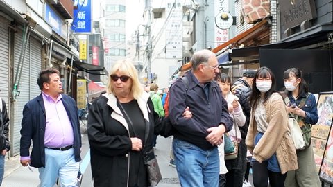 Tokyo, Japan - March 31, 2019: Street in Tsukiji near Ginza with many crowd people walking in market by sushi food vendors stalls taking pictures in slow motion