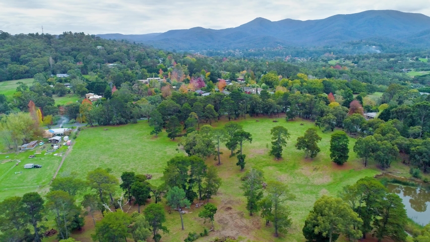 Aerial pan across grass, pond  and trees with mountains on the horizon. Scenic suburban area of Healesville, Victoria, Australia