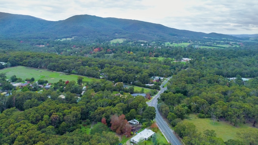 Backward drone flight in beautiful countryside homes surrounded by trees and mountains. Healesville, Victoria, Australia