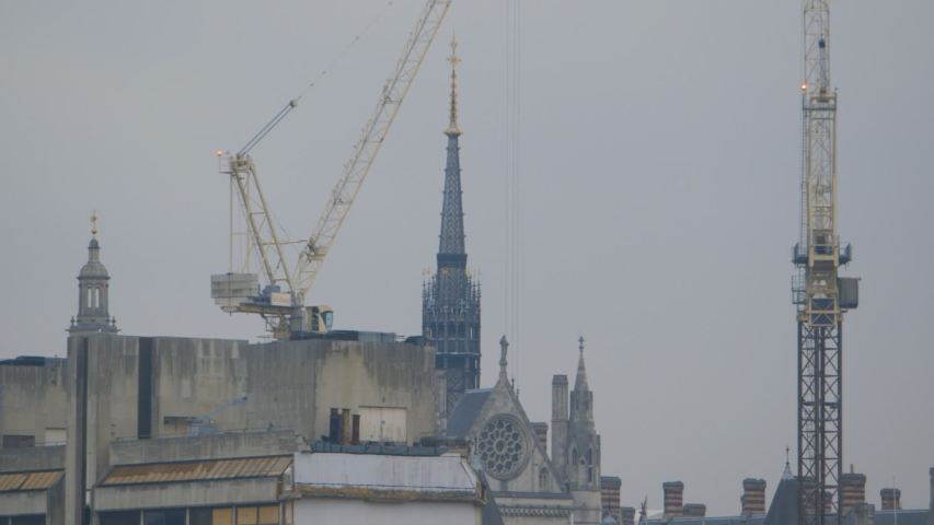 Steady, exterior, medium wide shot of the peak of a church building and two nearby cranes.