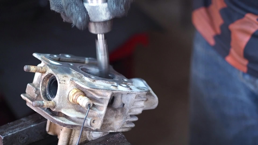 A motorcycle mechanic is repairing the cylinder head of a motorcycle.