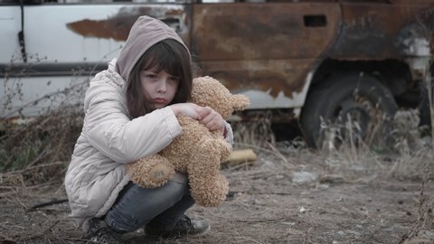 Homeless child with a toy. Sad little slum girl hugs bear cub.