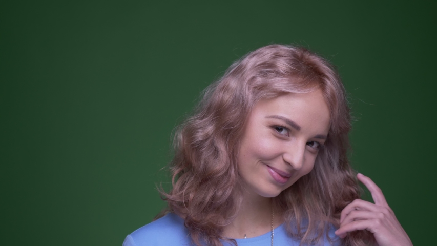 Beautiful model with wavy long hair plays with her hair flirting with camera on green chroma background.