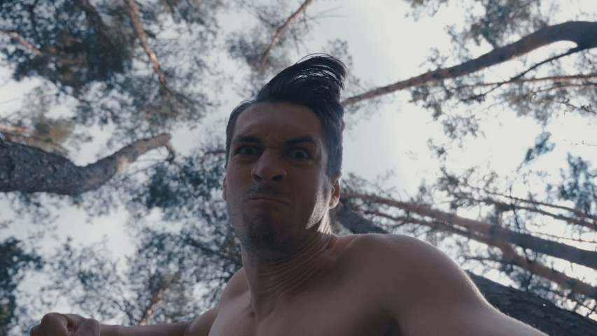 Furious aggressive man beats with his fists the lying person outdoor at forest