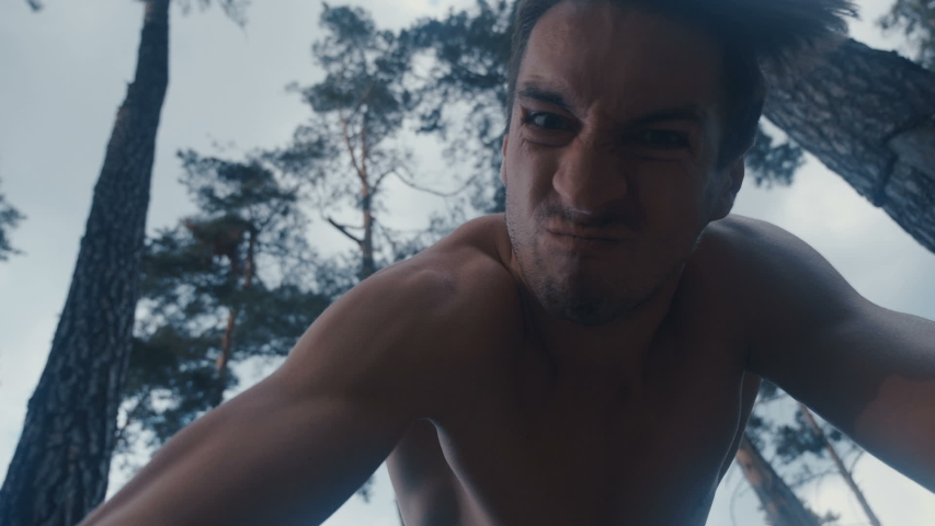Furious aggressive man beats with his fists the lying person outdoor at forest