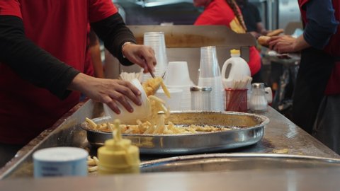 Kitchen worker at foodtruck at festival or street vendor serves french fries, fried potatoes or wedges into individual serving cups. Concept fast food, calories and saturated oils and sugars industry