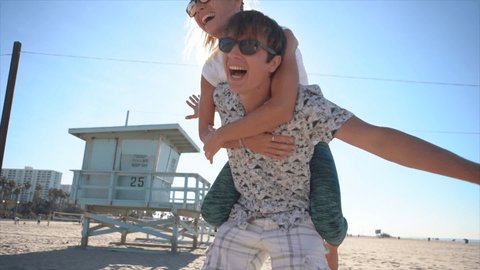 Piggy back at the beach. Young couple having fun at Santa Monica beach Los Angeles. Slow motion 