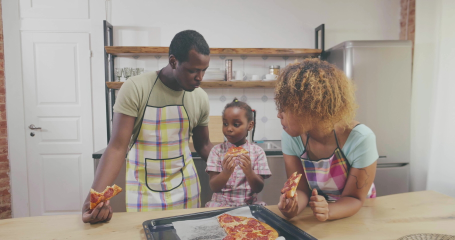 Happy African family Eating Pizza in Kitchen. Modern Kitchen at Home. Man Using Kitchenware. Young Family. Wooden Table in Kitchen. Food on Table. Royalty-Free Stock Footage #1029606239