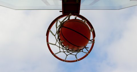 Upward view of basketball going through basketball hoop in basketball court. Sky and cloud in the background 4k