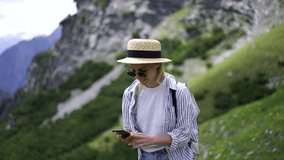 Smiling hipster girl in casual wear using smartphone camera making photos of nature landscape in mountains, young female wanderlust exploring National Park on vacations taking photos for travel blog