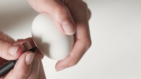 An unrecognizable woman holding a marker draws hearts in black on a broken egg for the Easter holiday. For the concept of Easter holidays. close-up hands draw a black marker on the egg