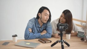Slow motion, Young Asian man and woman are talking with the camera which standing on the wood table. the couple man and woman sitting in the home and record video clip. blogger and vlog concept.