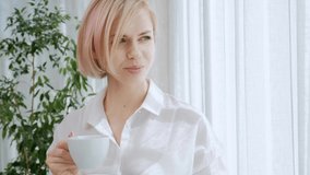 A young beautiful blond woman with short hair with glasses drinks coffee from a white cup in a light apartment. Office life, break, rest and relaxation. - Powered by Shutterstock - Get 15% off with code: PIKWIZARD15