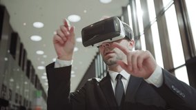 Modern middle aged businessman in formal suit and tie wearing VR headset, exploring and swiping data visualized in virtual reality in sunlight