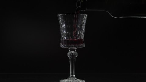 Wine. Red wine pouring in wine glass over black background. Rose wine pour from the bottle. Silhouette. Close up shot. Slow motion