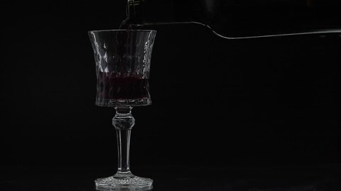 Wine. Red wine pouring in wine glass over black background. Rose wine pour from the bottle. Silhouette. Close up shot. Slow motion
