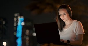 Young female student with laptop at night in town typing text