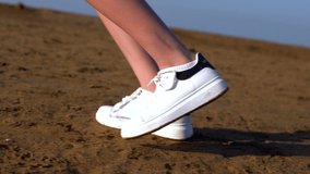 Feet and sneakers of a young woman on a beach