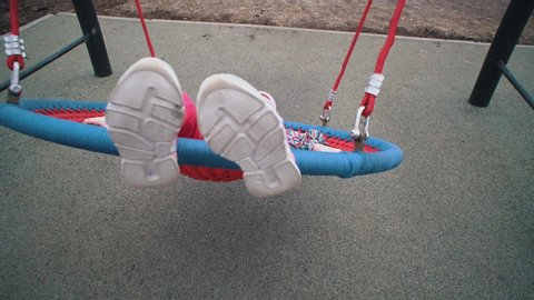 Little cute girl swinging on round swing with tight weave rope platform seat in park on cloudy day.