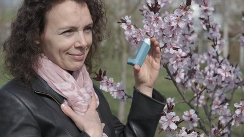 Asthma. Happy woman with inhaler in blooming sakura.