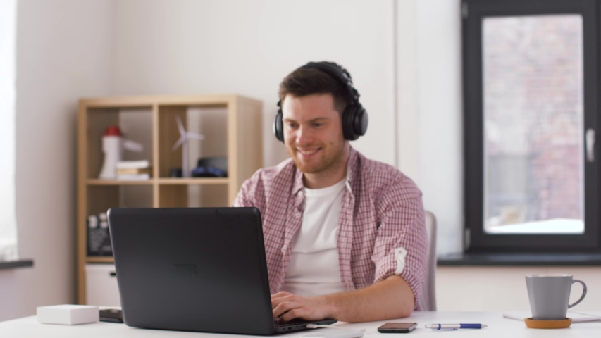 Technology, internet and people concept - happy young man in headphones with laptop computer celebrating success and dancing at office | Shutterstock HD Video #1029628880