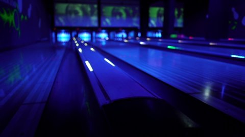 A bowling ball traveling down the lane and hitting pins at a Black Light UV Bowling alley.