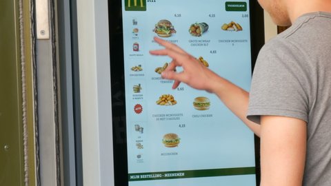 Amsterdam, Netherlands - April 21, 2019: A young man makes an order at McDonalds using a digital screen. Modern technologies of ordering food through a special service without operators