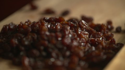 Slow motion footage of a bunch of raisins dropping into a pile on a wood cutting board