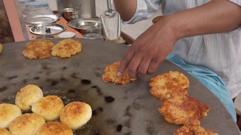 Slow-motion cooking of Aloo tikki or potato cutlet/ croquette on a large open pan, an Indian snack, comfort food of fried boiled potatoes, peas and various curry masala spices. handheld stabilized 4k