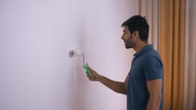Close-up video of a young Indian boy painting walls of the room white with a roller. Indian stock footage of a man wearing casualwear painting walls of his new house with roller - Shifting to a new...